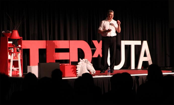 Man, in formal attire, speaking to audience at TEDxUTA