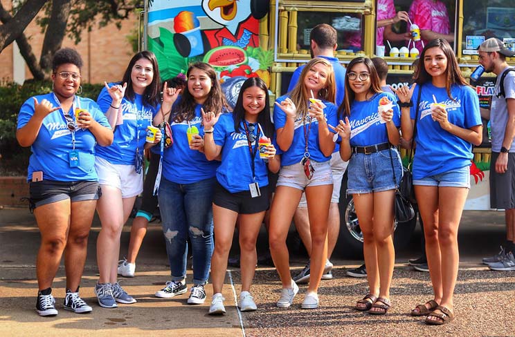 7 women standing in front of a Kona Ice truck holding snow cones and Maving up