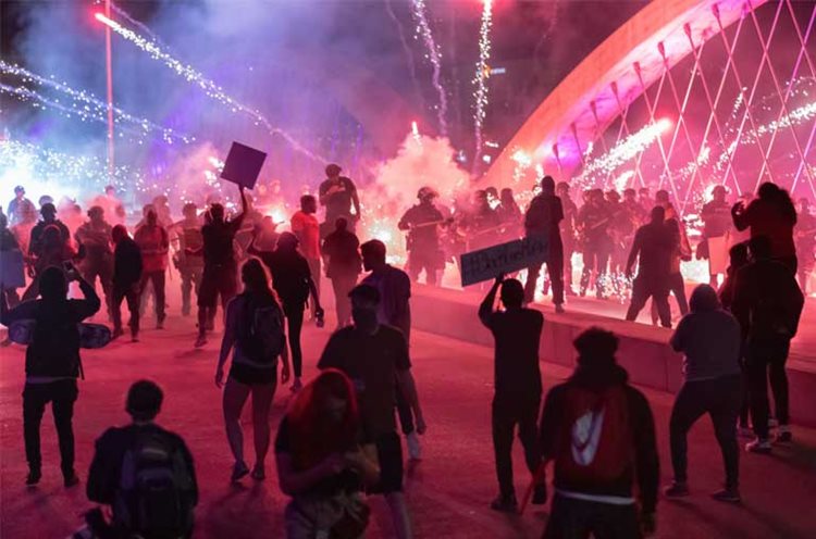 Large group of people spread out in dark silhouettes at night with bright lights in the background